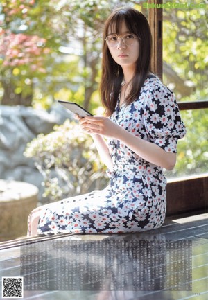 A woman with long black hair standing in front of a wall.