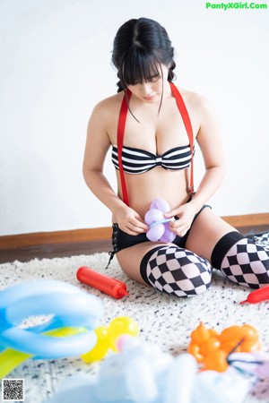 A woman sitting on the floor holding a bunch of balloons.