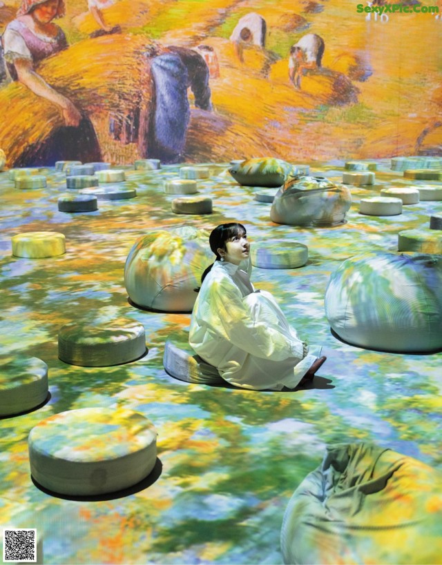 A woman sitting on a bean bag chair in front of a painting.