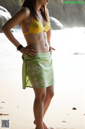 A naked asian woman standing in the ocean on a beach.