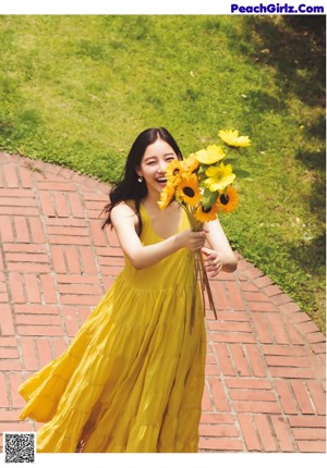 A woman in a yellow dress holding a bunch of sunflowers.