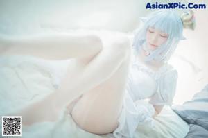 A woman in a white dress sitting on a wooden floor.