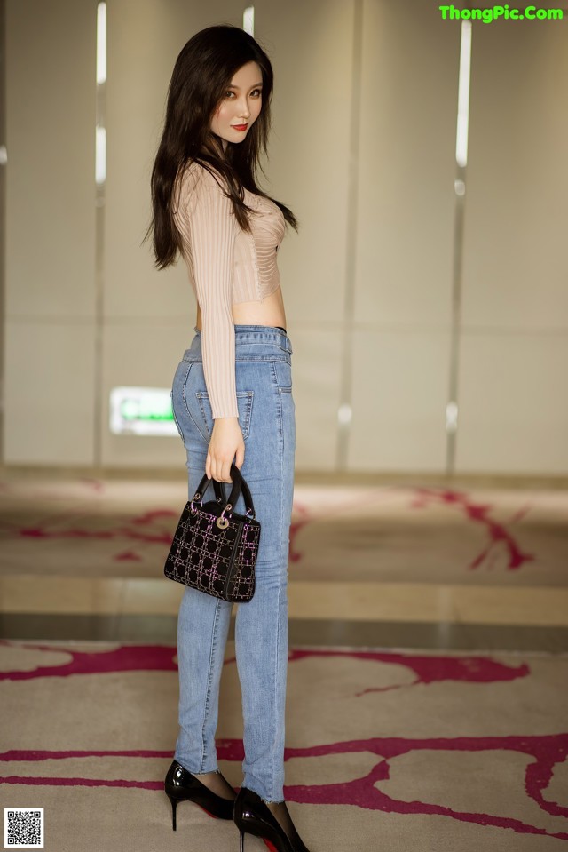 A woman standing in a hallway holding a handbag.