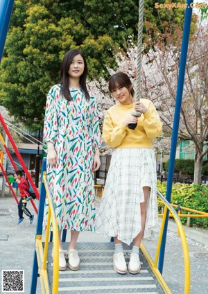 Two young women standing next to each other on a swing.