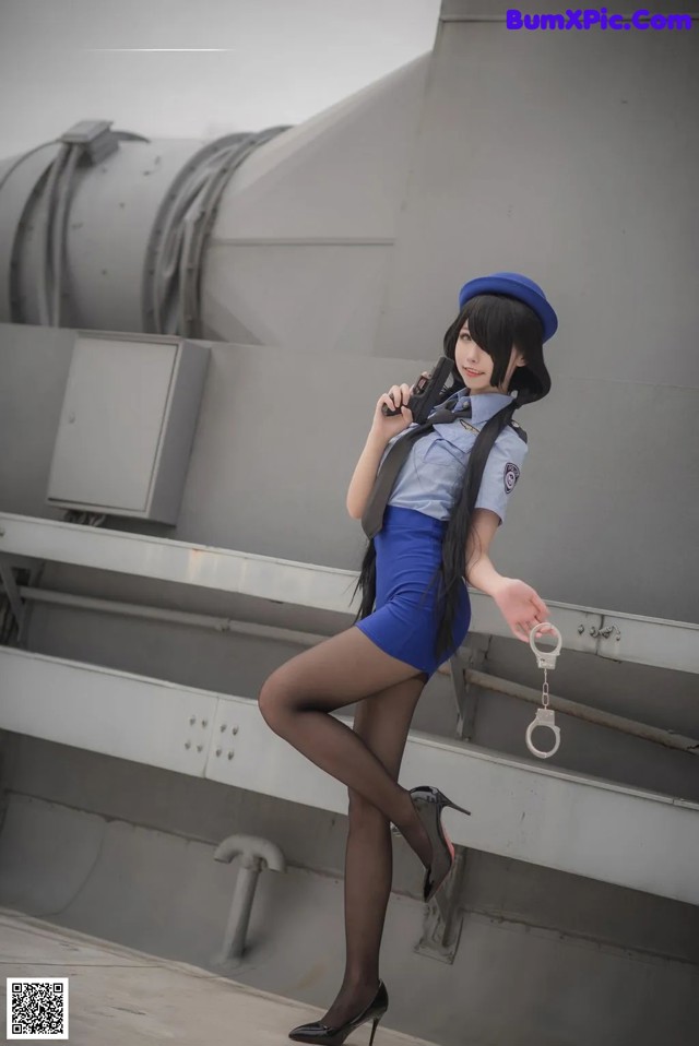 A woman in a blue dress and hat holding a gun.