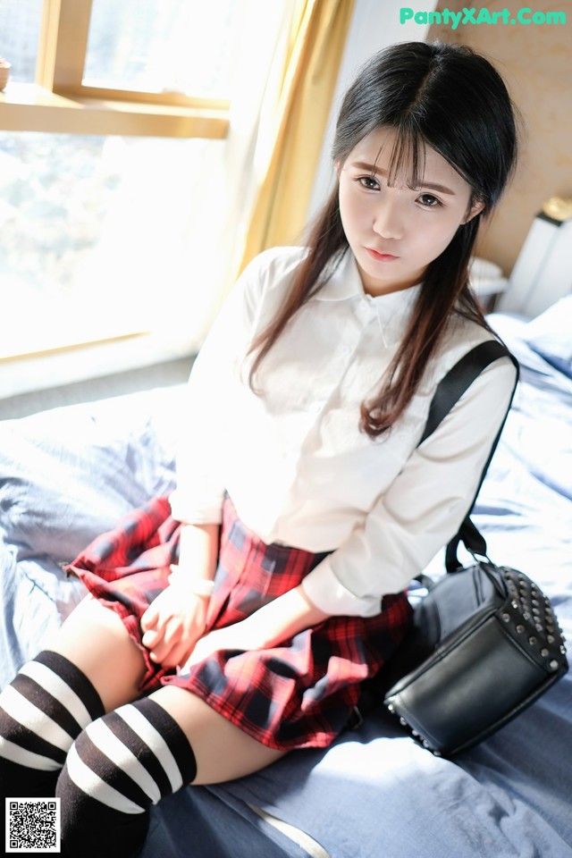 A woman in a school uniform sitting on a bed.