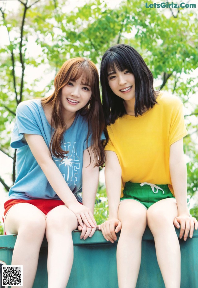 Two young women sitting on top of a green trash can.