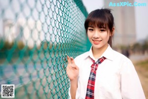 A woman in a school uniform leaning against a tree.