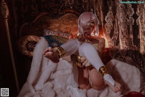 A woman in a white outfit is sitting on a bed.