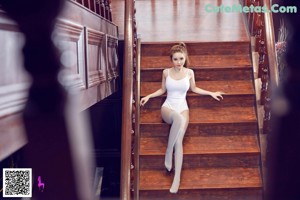 A woman in a white bodysuit standing on a wooden staircase.