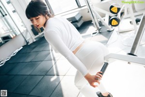 A woman in a white top and leggings working out in a gym.