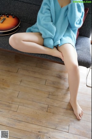 A woman sitting on a couch wearing a blue sweater.
