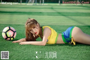 A woman in a red and yellow shirt is posing in front of a soccer goal.