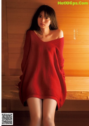 A woman in a red sweater laying on a bed.