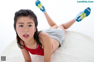 A woman in a red top and white shorts sitting on a white rug.