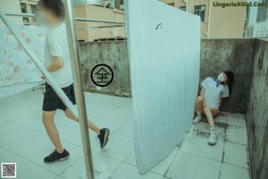 A naked woman sitting on the ground next to a building.