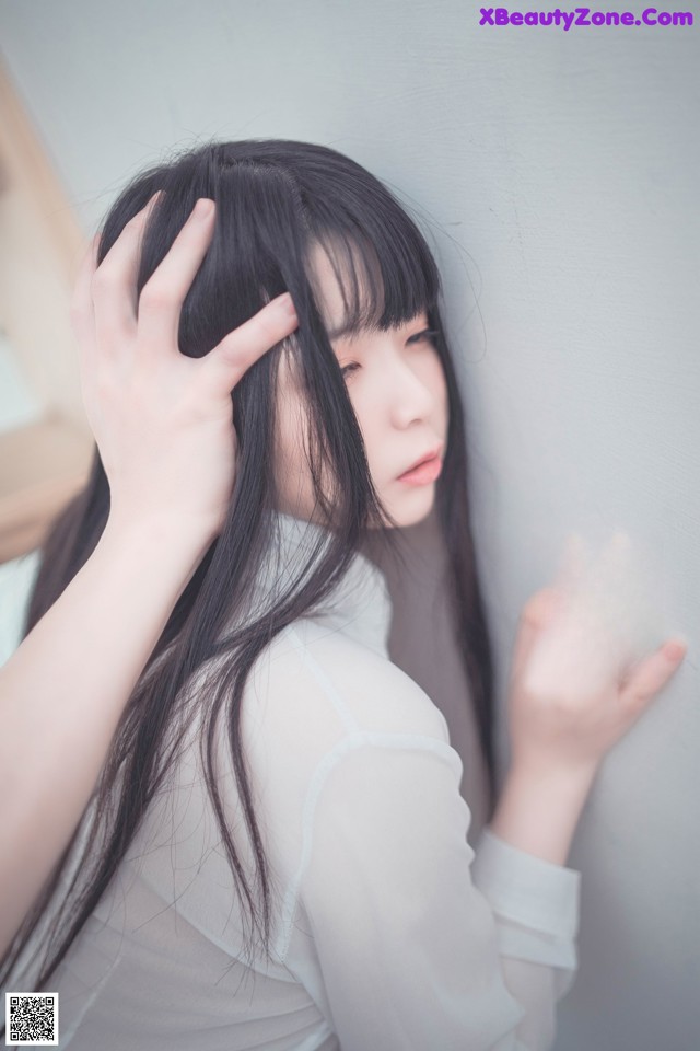 A woman with long black hair leaning against a wall.