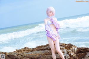 A woman in a bikini standing on a rock by the ocean.