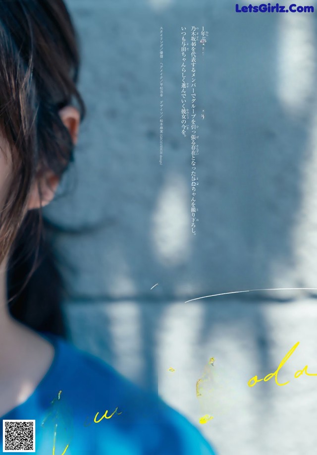 A woman in a blue dress standing in front of a wall.