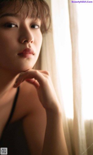 A woman in a black tank top looking out a window.