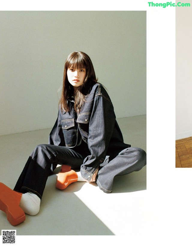 A woman sitting on the floor wearing a denim jacket and jeans.