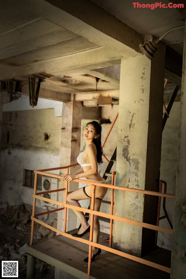 A woman in a white bra and fishnet stockings posing on a railing.